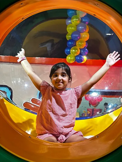 A happy girl peeks out from a transparent tube slide, one of the many exciting ways to travel through our play maze.