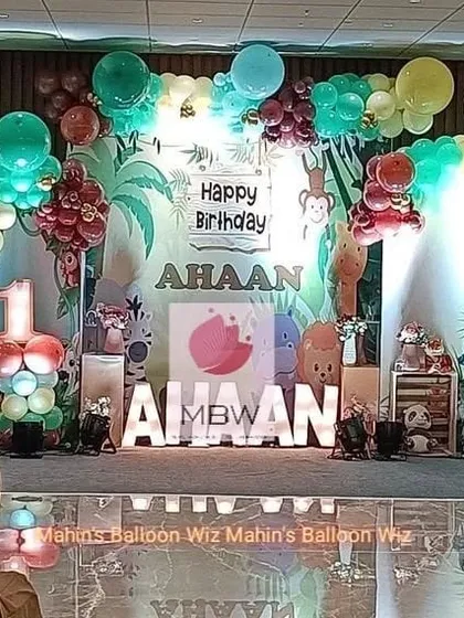 A wild jungle-themed birthday with a lush, illustrated backdrop. The stage is filled with animal props and a balloon garland in jungle-inspired colors.