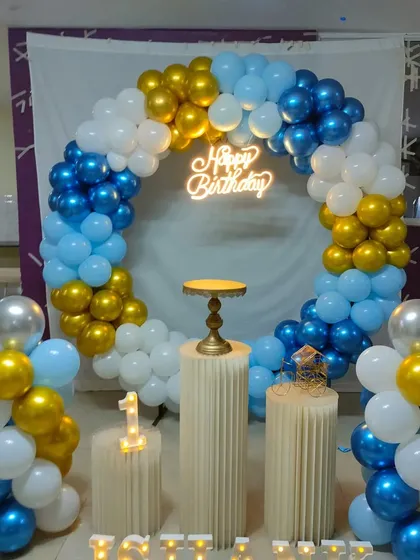 A blue, white, and gold balloon arch with pedestals for a first birthday celebration.