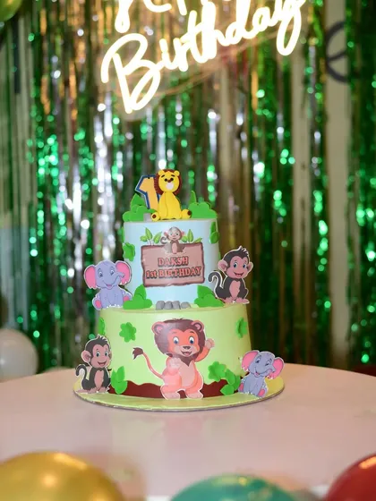 A detailed look at a jungle-themed first birthday cake. It features adorable fondant animals like a lion, monkeys, and elephants.