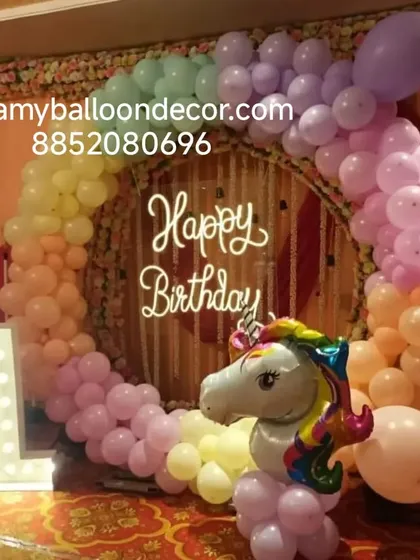 A pastel rainbow unicorn theme for a first birthday party. The setup includes a beautiful balloon ring, a large unicorn foil balloon, and a light-up marquee number '1'.