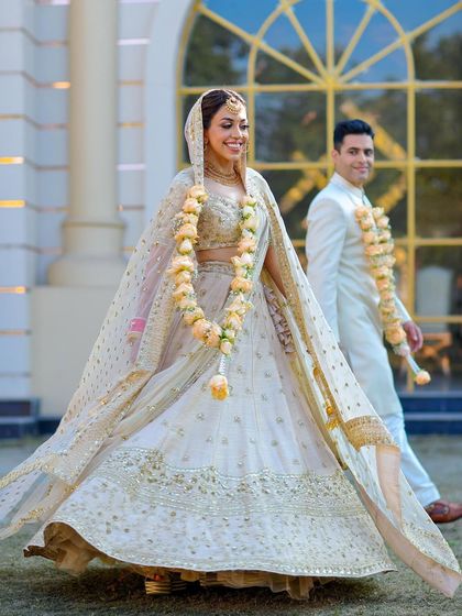 A dynamic shot of the bride twirling in her white lehenga, with the groom walking behind her, capturing movement and happiness.