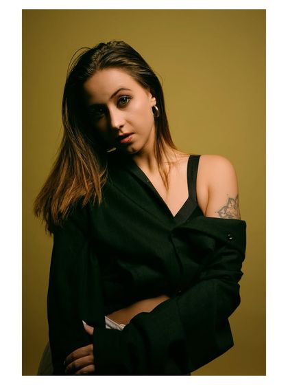 A moody and atmospheric fashion portrait. The dark, off-the-shoulder top and the subject's intense gaze create a feeling of quiet confidence and mystery.