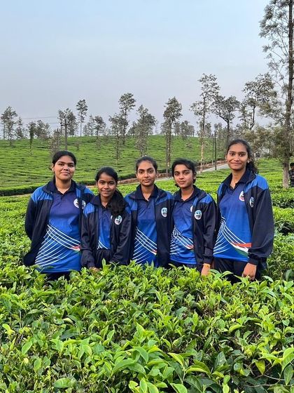 A team of girls in matching jackets stands together in the tea fields, a memory of their time at the Barapole camp.