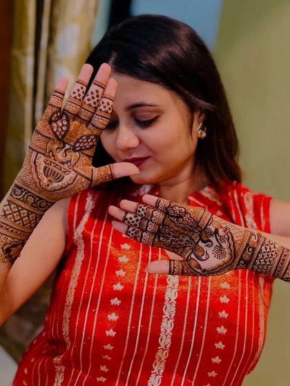 A client posing to show off her unique peacock-themed mehendi, with one hand featuring a full peacock and the other with feather details.