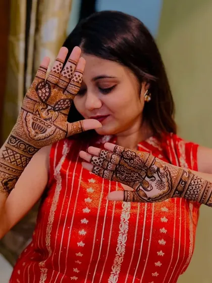 A client admiring her fresh mehendi. The design features classic peacock motifs, and she is beautifully framing her face with her henna-covered hands.