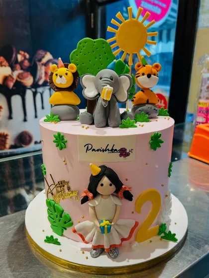 A sweet pink jungle-themed cake for a 2nd birthday, combining a cute girl figurine with fondant animals.