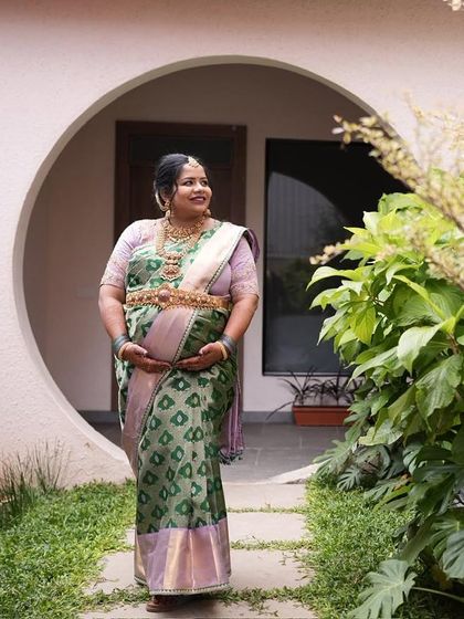 Pavithra walking through a garden, the soft light highlighting the gentle sheen of her silk saree. This is elegance perfected for a Seemantham ceremony.
