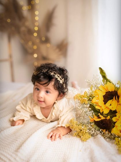 A bright-eyed baby girl lies next to a sunflower during her five-month photoshoot. The natural elements add a touch of sunshine to the session.