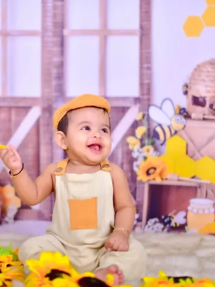 A cheerful baby in a honeybee-themed setup, surrounded by sunflowers and bee props.