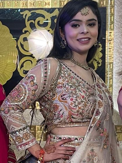 A close-up of a happy client in a beautiful ivory lehenga with colorful paisley embroidery. The sheer sleeves with detailed work are a lovely touch.