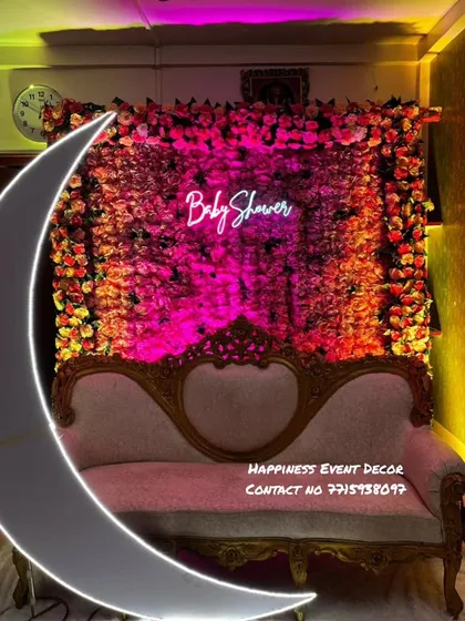For more intimate home functions, I can create beautiful backdrops like this one. This baby shower setup features a dense wall of artificial flowers, a custom 'Baby Shower' neon sign for a modern touch, and an elegant sofa, perfect for photos.