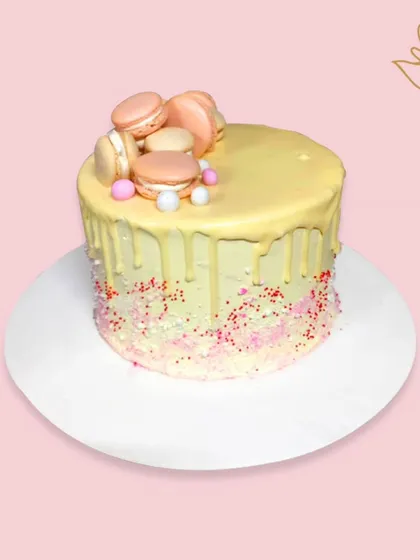 A delightful macaron drip cake with a white chocolate drip and colorful sprinkles. The crown of macarons on top makes this a chic and delicious treat.