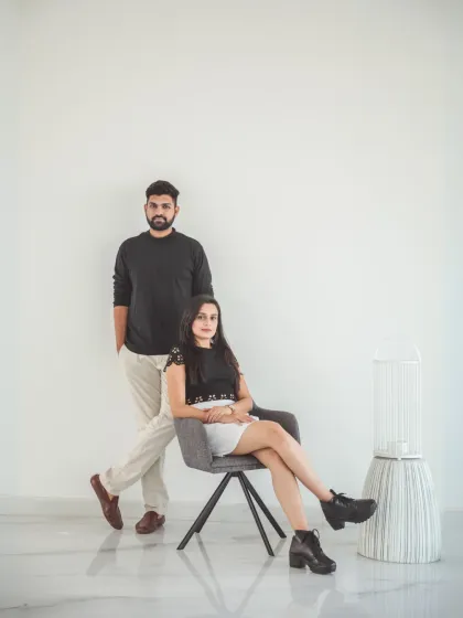 A minimalist and modern portrait against a clean white wall. The couple's coordinated black and white outfits and the simple composition create a chic and stylish pre-wedding photograph.
