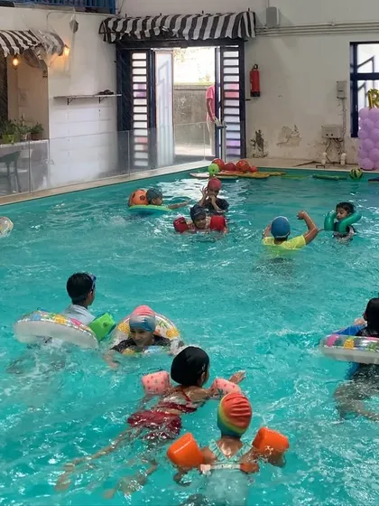 Another angle of a lively pool party, with the cafe and seating area visible in the background, where parents can supervise in comfort.