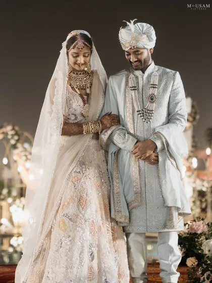 A gentle moment between the bride and groom. Her arm linked through his, they share a quiet, downward glance, a picture of serene togetherness amidst the wedding festivities.