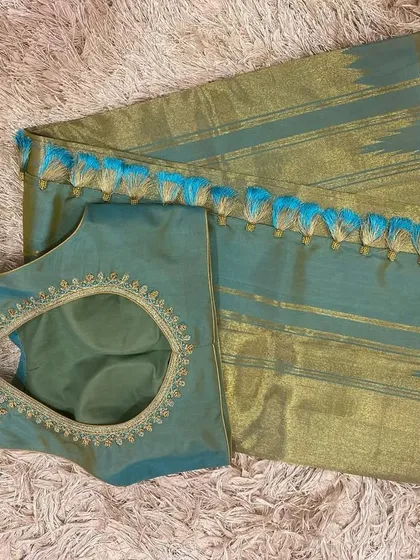 A teal and gold-toned silk saree paired with a matching teal blouse. The blouse features a simple embroidered neckline and a keyhole back.