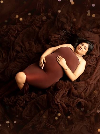 An aerial shot that showcases the texture and volume of the gown. The expecting mother lies peacefully on a bed of brown tulle, with sparkling lights adding a magical touch.
