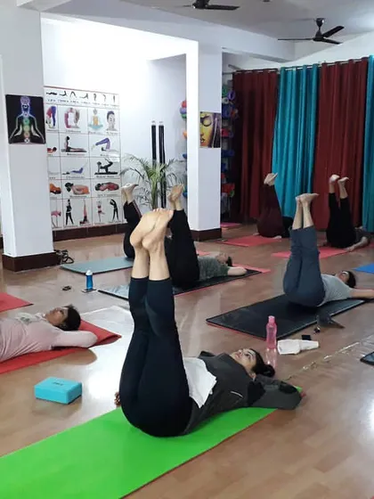 A group working on an inverted leg lift, a preparatory exercise for poses like Sarvangasana (Shoulder Stand). This helps build core strength and body awareness.
