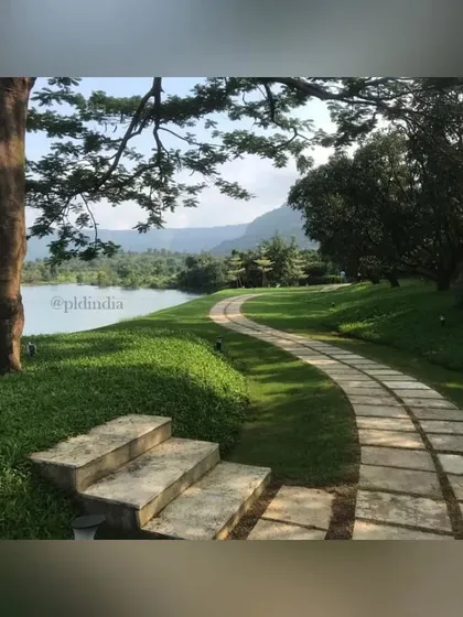 The pathway winds under the canopy of a large rain tree, offering a shady spot to pause and enjoy the view. The steps are made of rough-hewn stone, adding to the naturalistic feel.