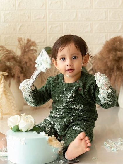 This little one is all in, with frosting-covered hands and a look of pure joy during his green-themed boho cake smash.