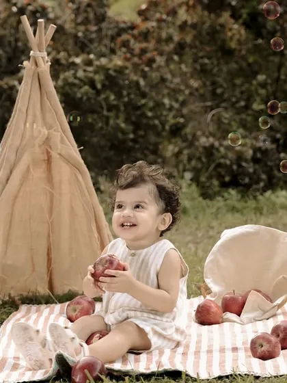 A baby boy smiles with delight during his outdoor picnic-themed first birthday shoot, complete with a teepee and bubbles. This shot captures the joy of a simple, beautiful celebration.