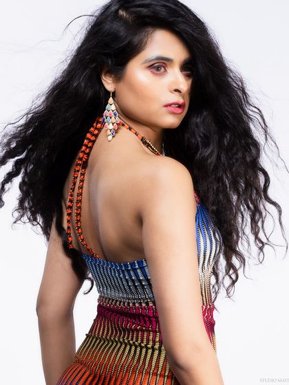 A profile shot of a model in a colorful striped dress, with a focus on her earrings and curly hair.
