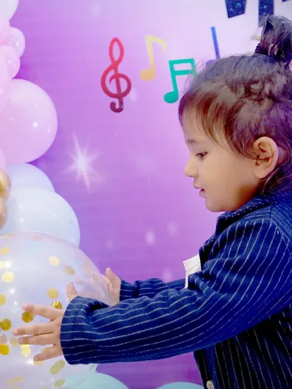 A candid side-profile of a young boy interacting with a confetti balloon at his party, showing a moment of genuine curiosity and play.