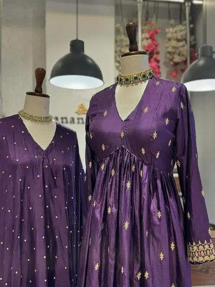 A detailed shot of two purple kurtas, one with a dotted pattern and the other with intricate star-like embroidery, both paired with elegant green-beaded chokers.