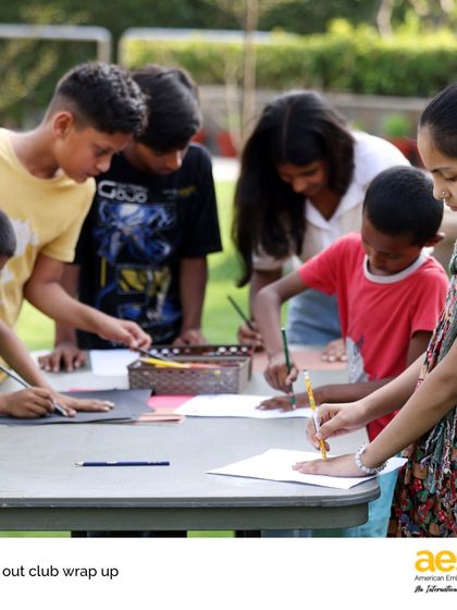 AES student volunteers help younger children with an art project during a 'Reach Out!' club session. These activities provide a creative outlet and build meaningful relationships.