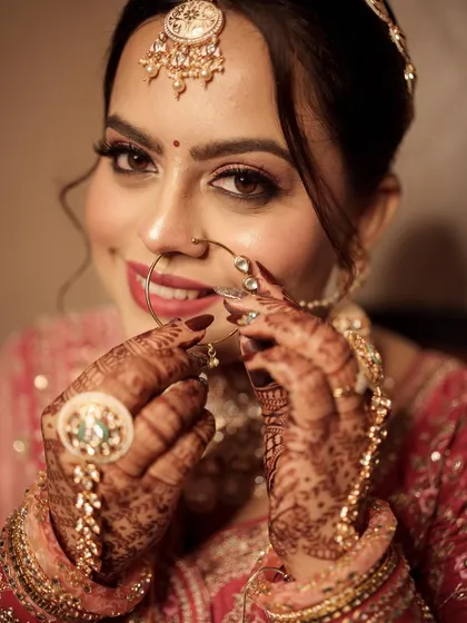 A close-up of the bride playing with her nath. The rose gold makeup looks stunning against her intricate henna.