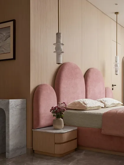 The custom bed for this kid's room features a series of soft, arched headboards in pink velvet. This playful design is balanced by the clean lines of the light wood veneer and the sculptural marble side table.