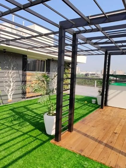 A daytime view of the pergola and deck area, showing the shadow patterns created by the roof and the lushness of the vertical garden.