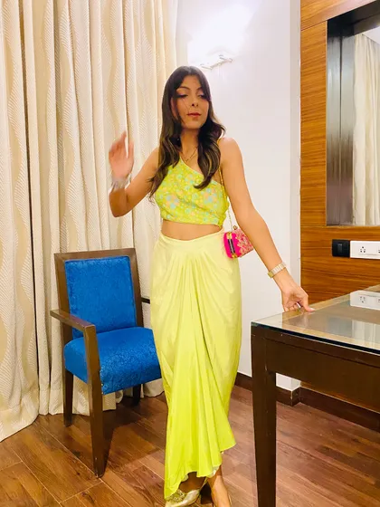 A full-length view of the lime green fusion outfit. The asymmetrical top and draped skirt create a flattering silhouette. It's a great example of a contemporary ethnic look for a modern wedding event.