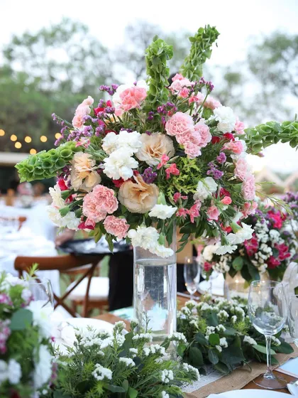 An elegant and lush centerpiece for a dining table. A tall glass vase holds a large bouquet of white and pink carnations with cascading bells of Ireland.