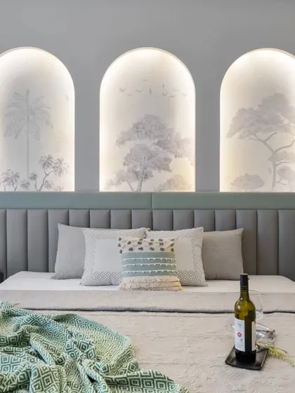 A master bedroom designed for tranquility, with a custom headboard featuring backlit arched niches with tropical wallpaper. The soft, layered textiles and calming color palette create a cozy and sophisticated sanctuary.