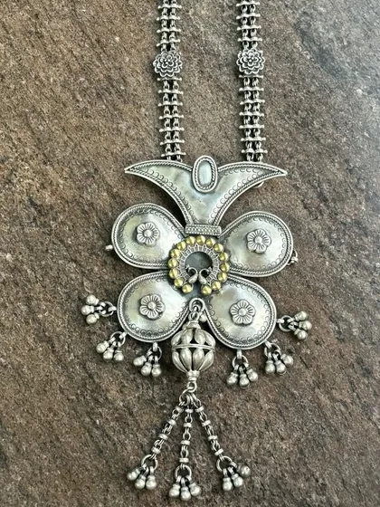 A unique oxidised silver pendant with a touch of gold. This large, floral-inspired piece has beautiful texture and detail, with dangling silver beads that add movement.