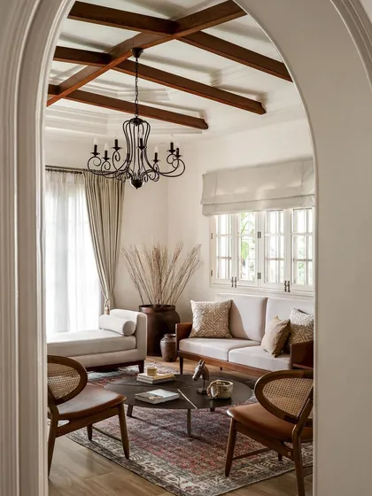 An arched view into the formal living room, where I designed a space with soaring ceilings and classic details. The exposed wooden beams and antique-style chandelier evoke a sense of grandeur, while the comfortable, modern furniture makes it feel livable.