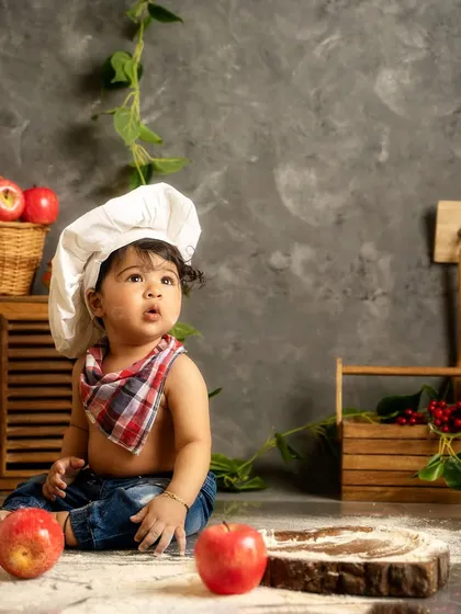 A moment of quiet contemplation for our baby chef. The rustic kitchen set, complete with apples and wooden crates, adds an authentic touch.