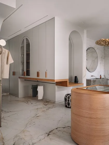 This walk-in wardrobe and bathroom was designed to feel like a high-end SoHo boutique. It features a sculptural, monolithic marble basin, an island dresser, and custom clothing racks, all set against a backdrop of luxurious veined marble.
