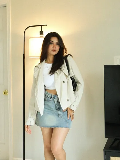 A full-length shot of a casual, transitional outfit. I've paired a denim mini-skirt with a white crop top and a light trench jacket, creating an accessible look for spring or fall.