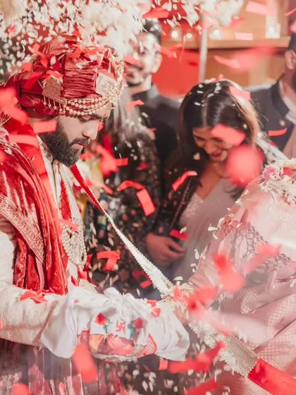 The couple taking their seven steps together, surrounded by the love and blessings of their family. The red confetti creates a vibrant and celebratory mood.