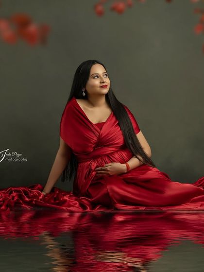 A beautiful composition featuring a mom-to-be in a red gown, seated with a water reflection effect. The soft red leaves at the top of the frame add depth and a touch of nature.