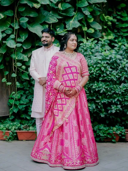 A classic, poised portrait of the couple against a lush green backdrop, showcasing their beautiful pink engagement outfits.