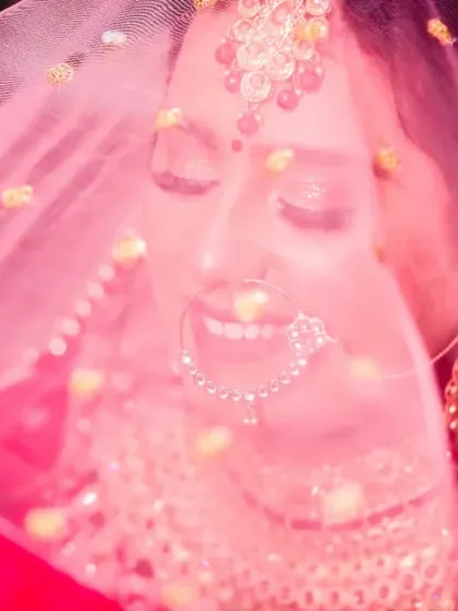 A dreamy and joyful bridal portrait. The bride is smiling with her eyes closed, seen through her pink veil, which creates a soft, romantic, and colourful effect.