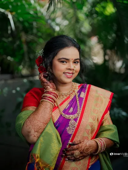 A beautiful portrait of the Maharashtrian bride, her hand gently touching her face. Her bright smile and traditional attire, including a nath and red flower in her hair, are highlighted.