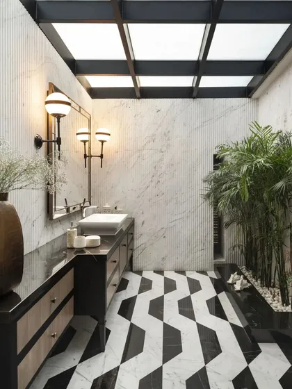 A stunning bathroom featuring a skylight, fluted marble walls, and a bold geometric-patterned floor. The space is designed to feel like a private spa, complete with natural elements like the indoor bamboo planter.