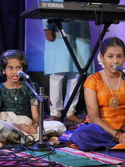 Two students sit cross legged on stage, singing a traditional Keertane. This setup is typical for many of our Indian classical and devotional performances.