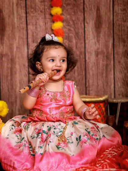 This little Radha is absolutely charming, nibbling on a flute in a beautiful pink and floral lehenga. We capture these candid moments that show your child's sweet personality.