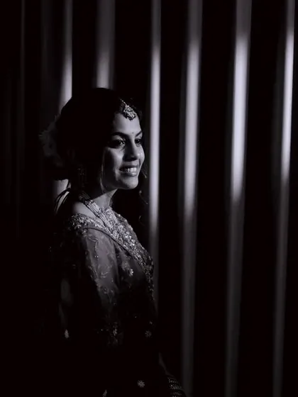 A moody black and white portrait of the bride against a curtain. The striped shadows add a graphic, artistic element to the shot.